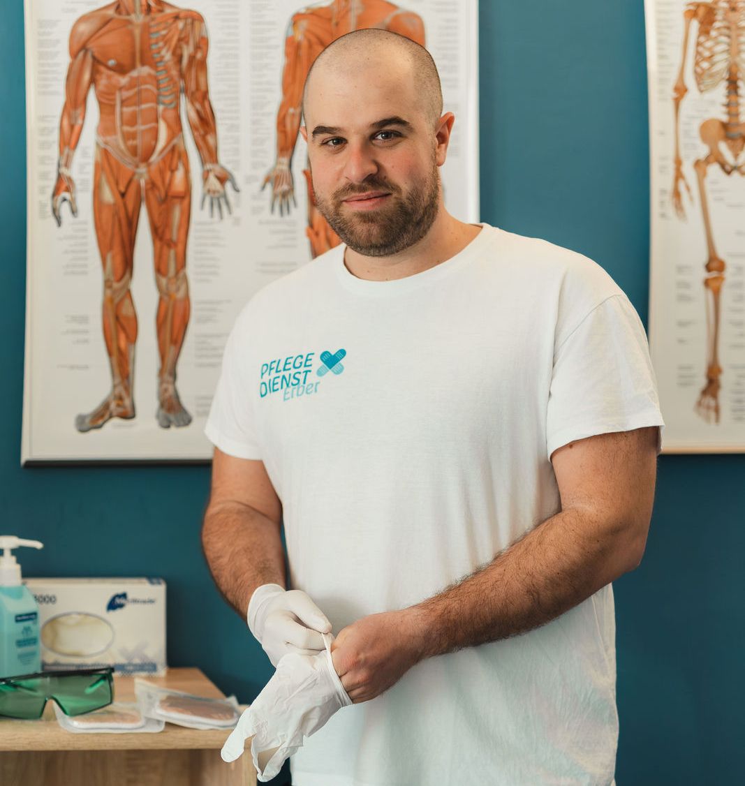 Ein Foto von DGKP Christian Erber vor einer blauen Wand. Auf dem T-Shirt ist das Logo von Pflegedienst Erber
